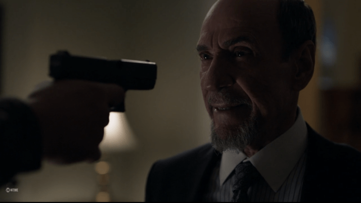 Elderly man (Dar) smiles, with a gun to his face