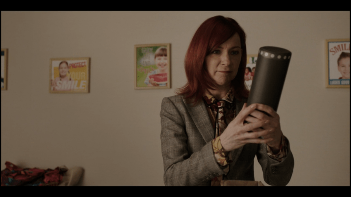 A red haired woman (Elsbeth) stares at her "Ada" device with affection.