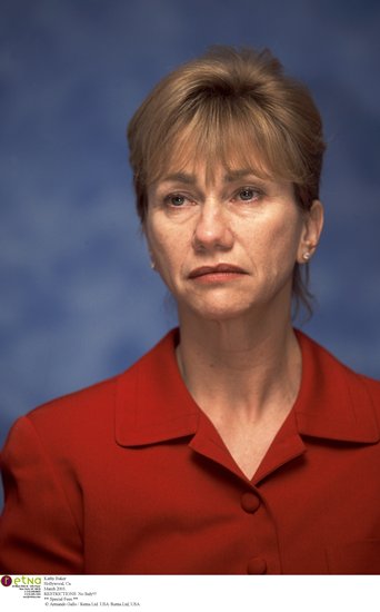 Kathy Baker, a white middle-aged woman, in a red suit on a blue background.