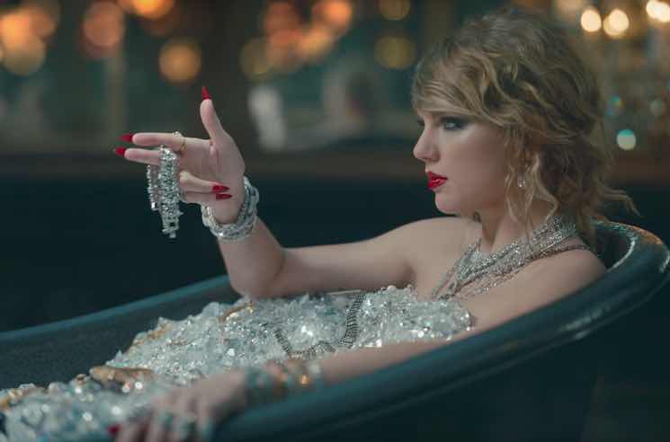 Screenshot from "Look What You Made Me Do" music video - Taylor Swift sits in bathtub, covered in diamonds, pointing fingers like a gun.