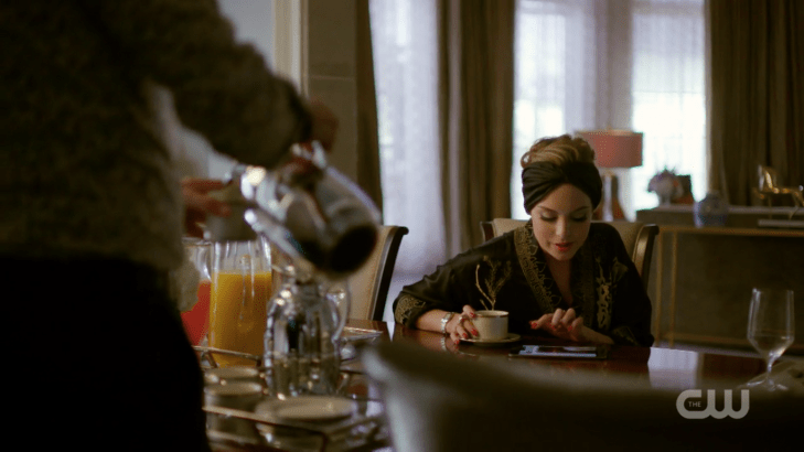 Fallon sits at the table with a tablet and a coffee mug, wearing a turban.