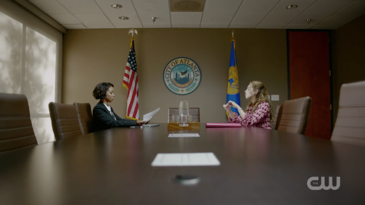 Two women (Fallon and Kori Rucks) sitting across from each other at a huge conference table in front of the seal of the city of Atlanta.
