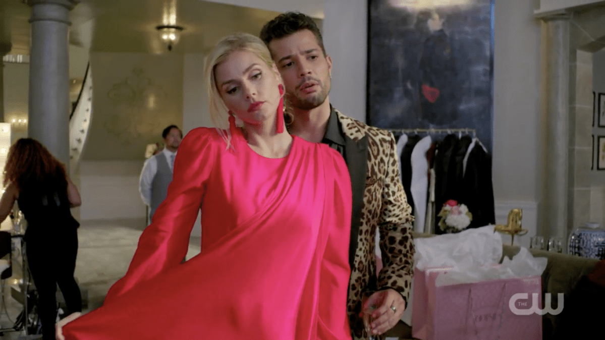 Sam and Claudia check themselves out in the mirror, Claudia in a fancy pink dress and earrings and Sam in a leopard-print jacket.