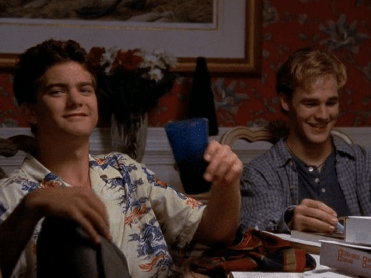 Pacey smirks while holding a cup of water, Dawson is laughing behind him.