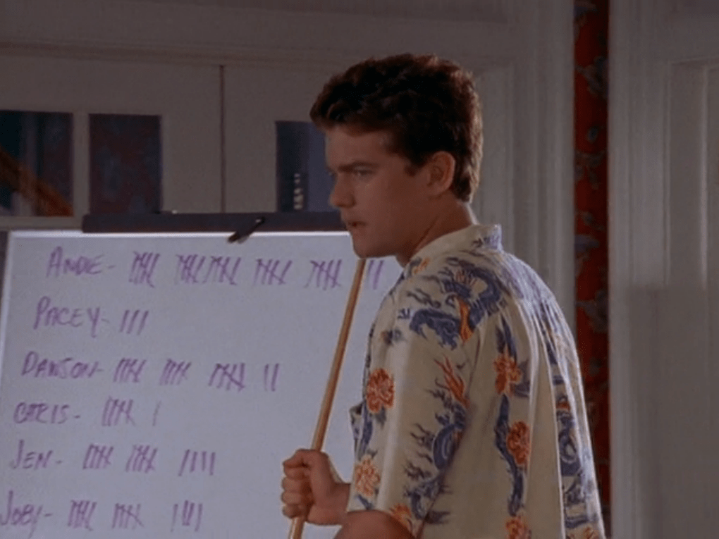 Pacey stands in front of an easel with tallies on it, holding a pointer.