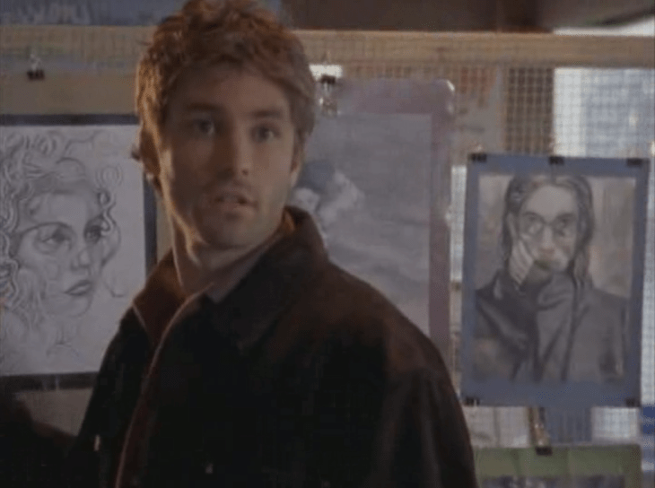 A white guy with light brown hair stands in front of Joey's drawings.
