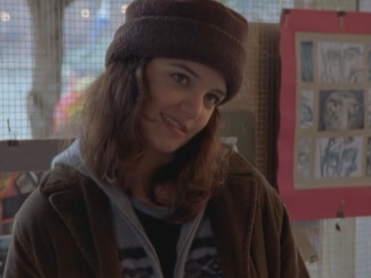 Joey wears a super cute brown hat, standing in front of her drawings.