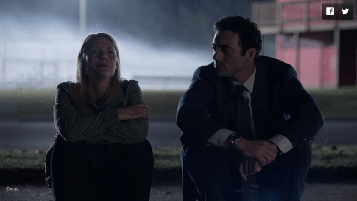 Carrie and Dante sit next to each other in front of a darkened field with light shining from above. Dante looks at Carrie while she looks tearfully upwards.