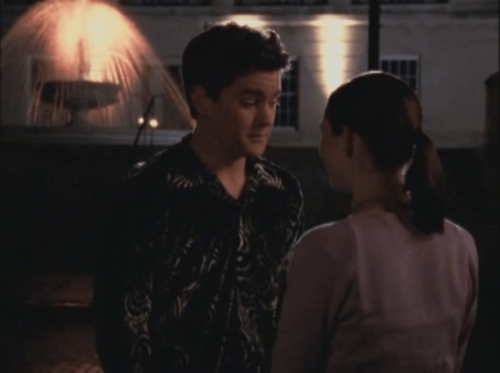 Pacey talks to Andie in front of a fountain while wearing a black velvet shirt with spirals pressed into it.