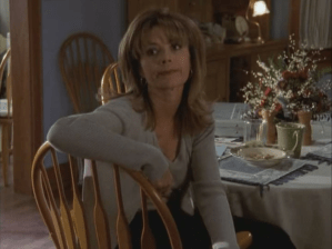 Gail sits in her kitchen with wispy bangs below her bouffant.