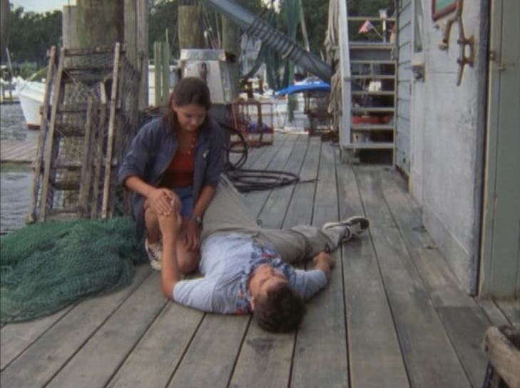 At the dock, Joey kneels over Pacey. He is lying flat on his back, patting her knee while she pats his hand.