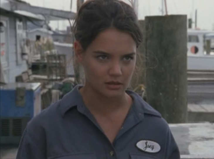 Joey, wearing a uniform shirt with a nametag, stands on the dock with an angry look.