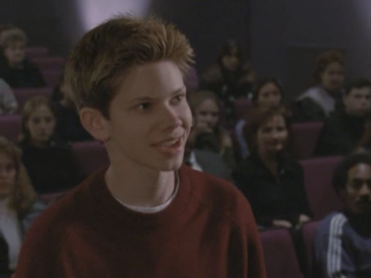 Shot of an actor who was on Boy Meets World standing in an auditorium in the audience, surrounded by a bunch of people.