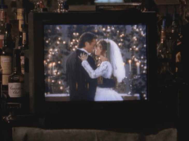 Old CRT television displaying a woman in a white veil (Gail) and a man with long curly hair reaching down to his collar (Mitch)