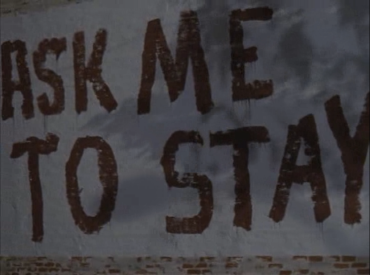 Picture of a brick wall painted white with black letters that say ASK ME TO STAY.