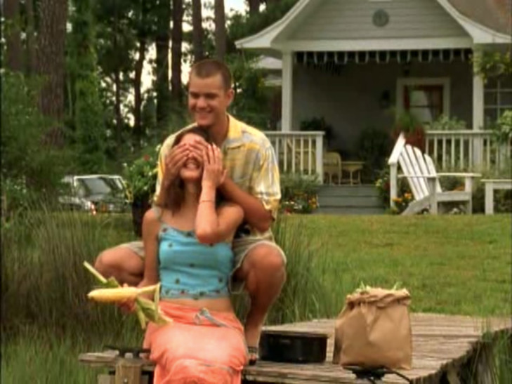 Out at the dock. Pacey kneels behind Joey grinning and covering her eyes with his hands. She's holding an ear of corn in one hand and holding his hand in the other, also grinning.