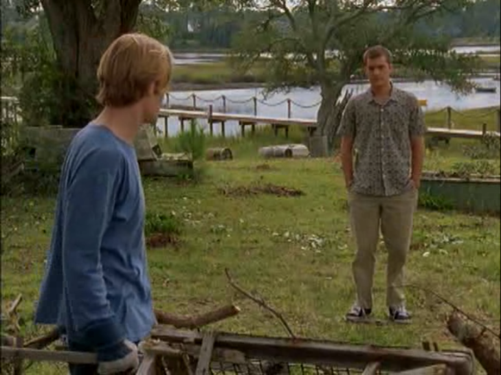 Exterior, daylight. Pacey (background) stands facing Dawson, hands in pockets, while Dawson works on some wood or something, facing away from camera (foreground).