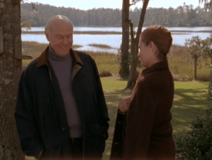 Exterior, day. Mr. Brooks and Grams stand in the yard. Brooks is wearing a coat over a wide-ribbed blue turtleneck sweater.