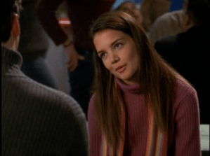 Joey tilts her head, wearing a magenta ribbed turtleneck with a scarf.