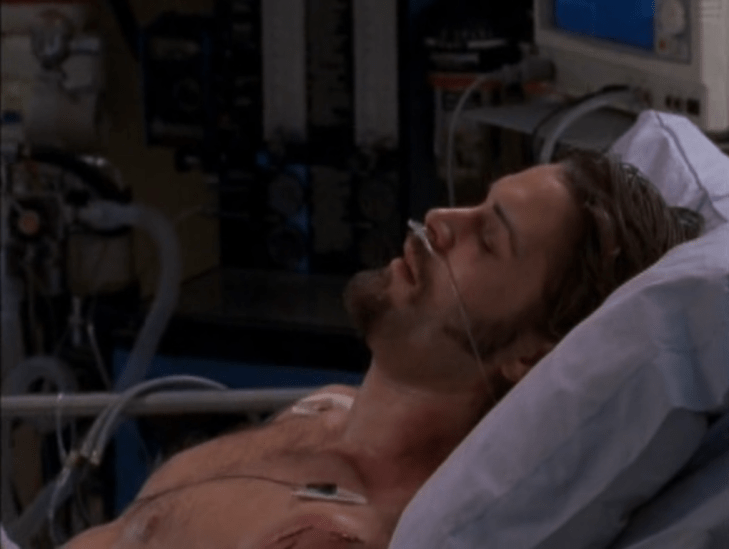 A bare-chested man lies in a hospital bed, zero bandages visible on his bust or face.