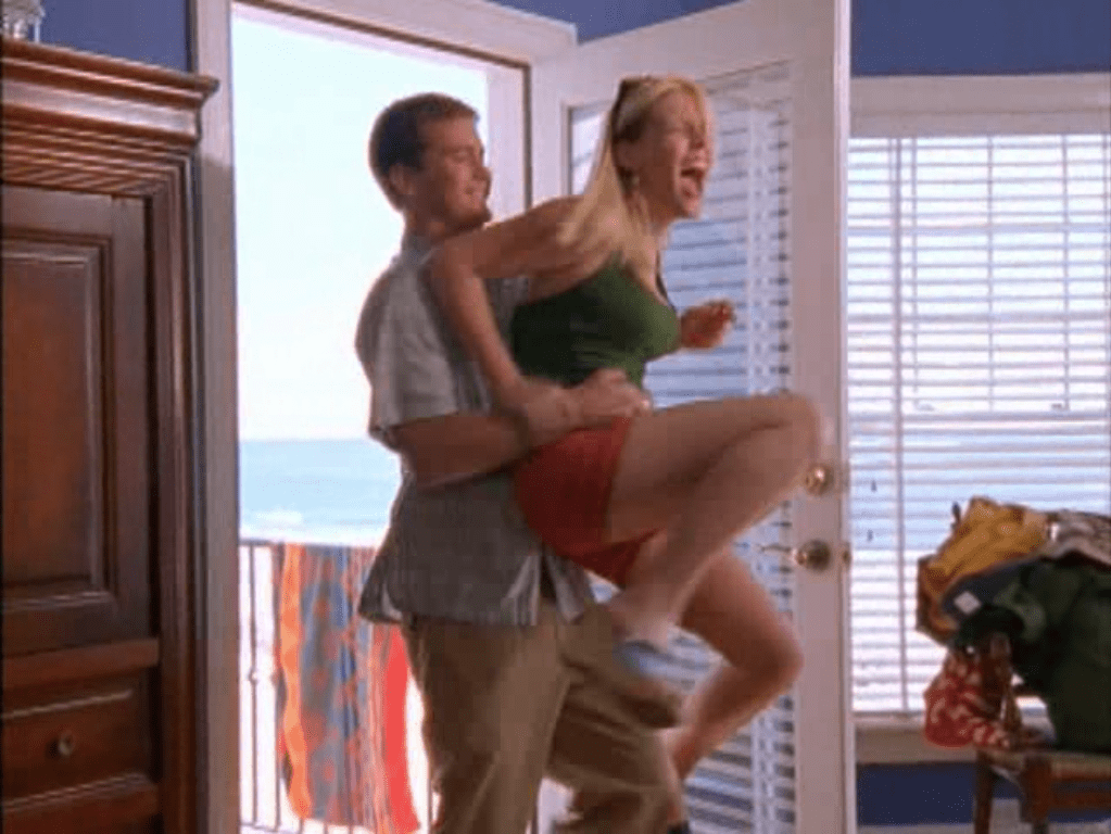 In a sunny room, Pacey holds Audrey up by the waist while she laughs and grabs his hand.