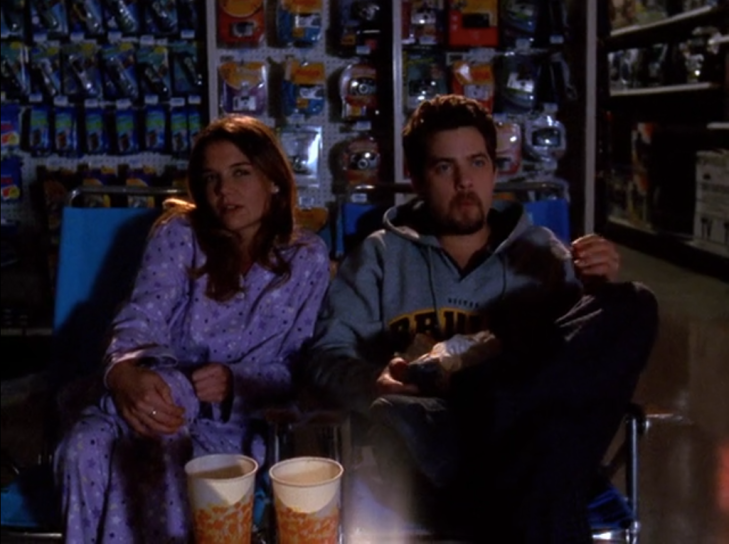 Joey and Pacey, wearing pajamas and sweatshirt respectively, are seen sitting on lawn chairs in a darkened store. Large soda cups in front of them. Pacey is chewing.