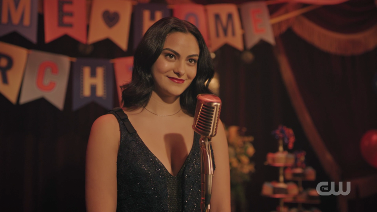 Veronica stands in front of a microphone in a sparkly dress, smiling.