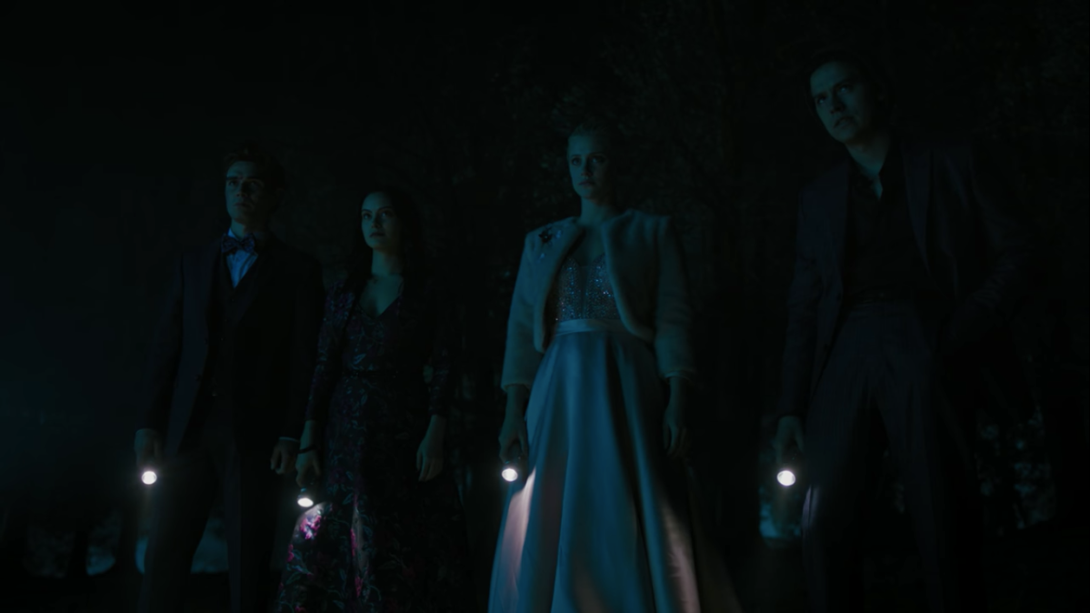 Archie, Veronica, Betty, and Jughead stand in the dark holding flashlights, dressed in formalwear.