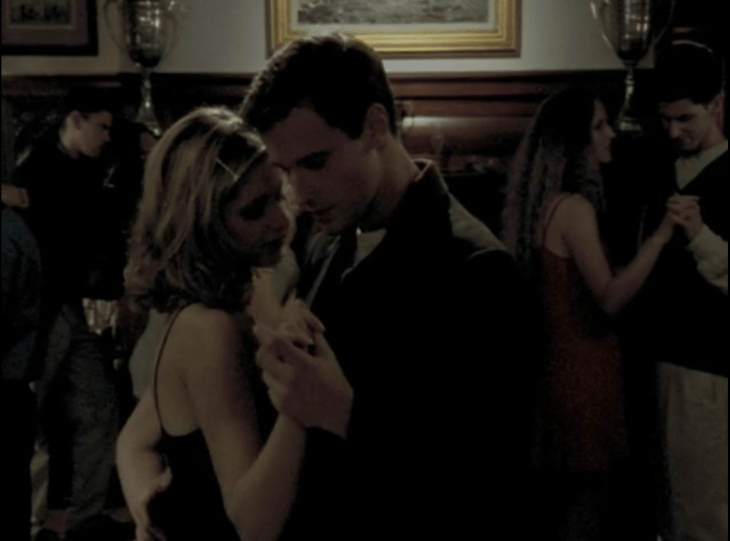 Buffy and a handsome young man dance, ballroom dancing style, in a room with several other young couples dancing around them.