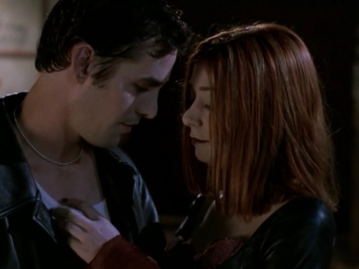 Willow and Xander, in vampire makeup and outfits, lean their heads close together with Willow's hand on Xander's chest.
