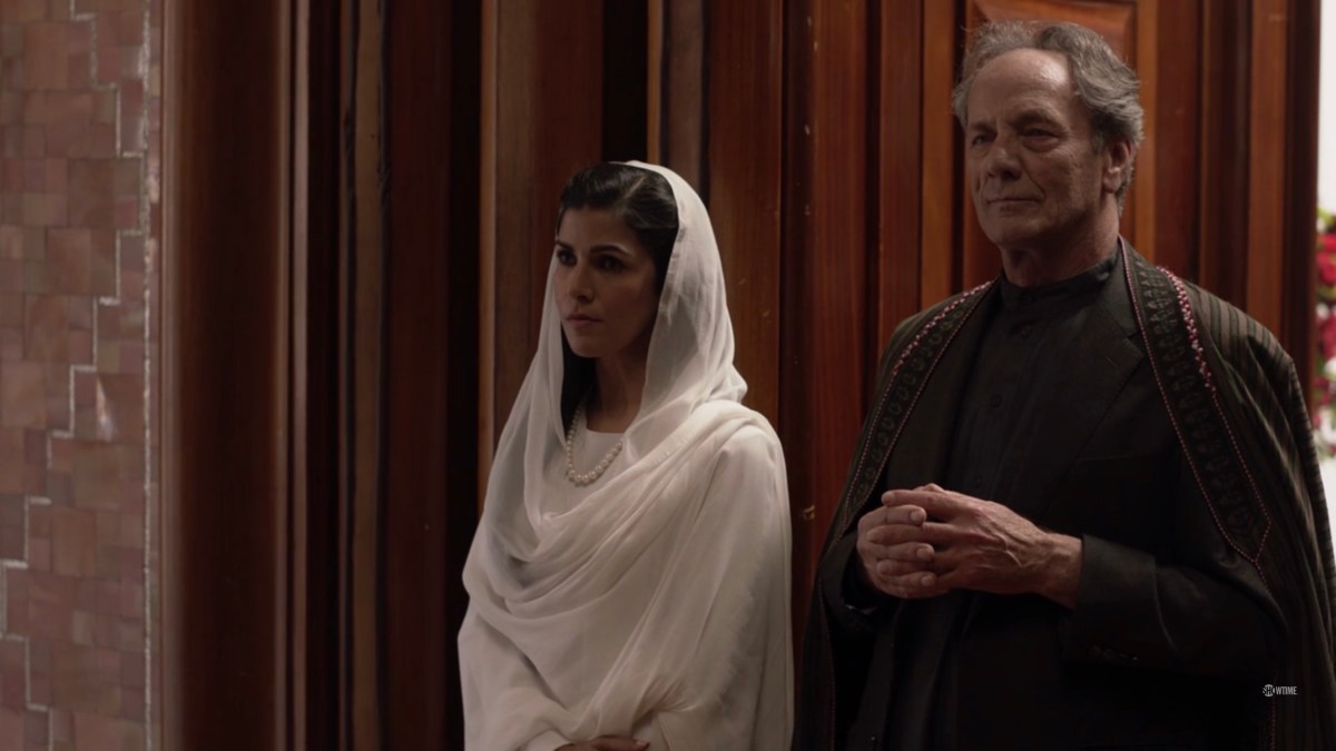 Tasneem, in a bright white outfit, and G'ulom stand in a corner looking cranky.