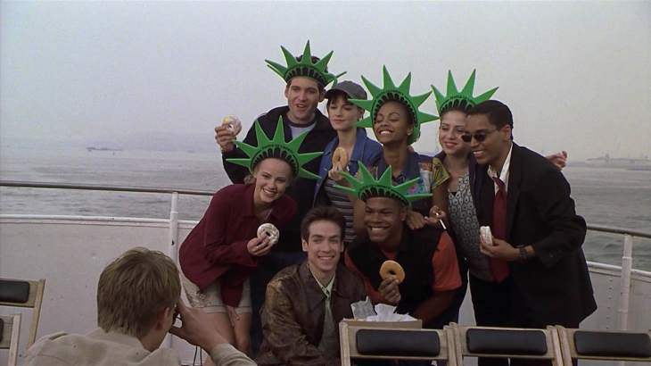 Image description: Eight people, most in Statue of Liberty hats and holding donuts, pose for a picture on a boat.