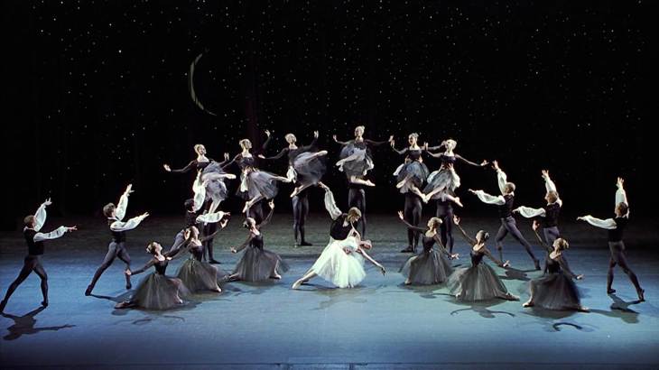 Image description: Onstage, many people dance with starlight in the background